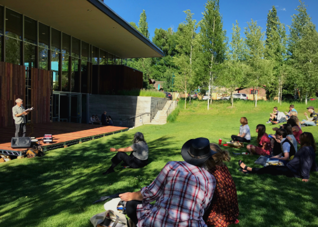 People sitting on a lawn watching an author read from his book